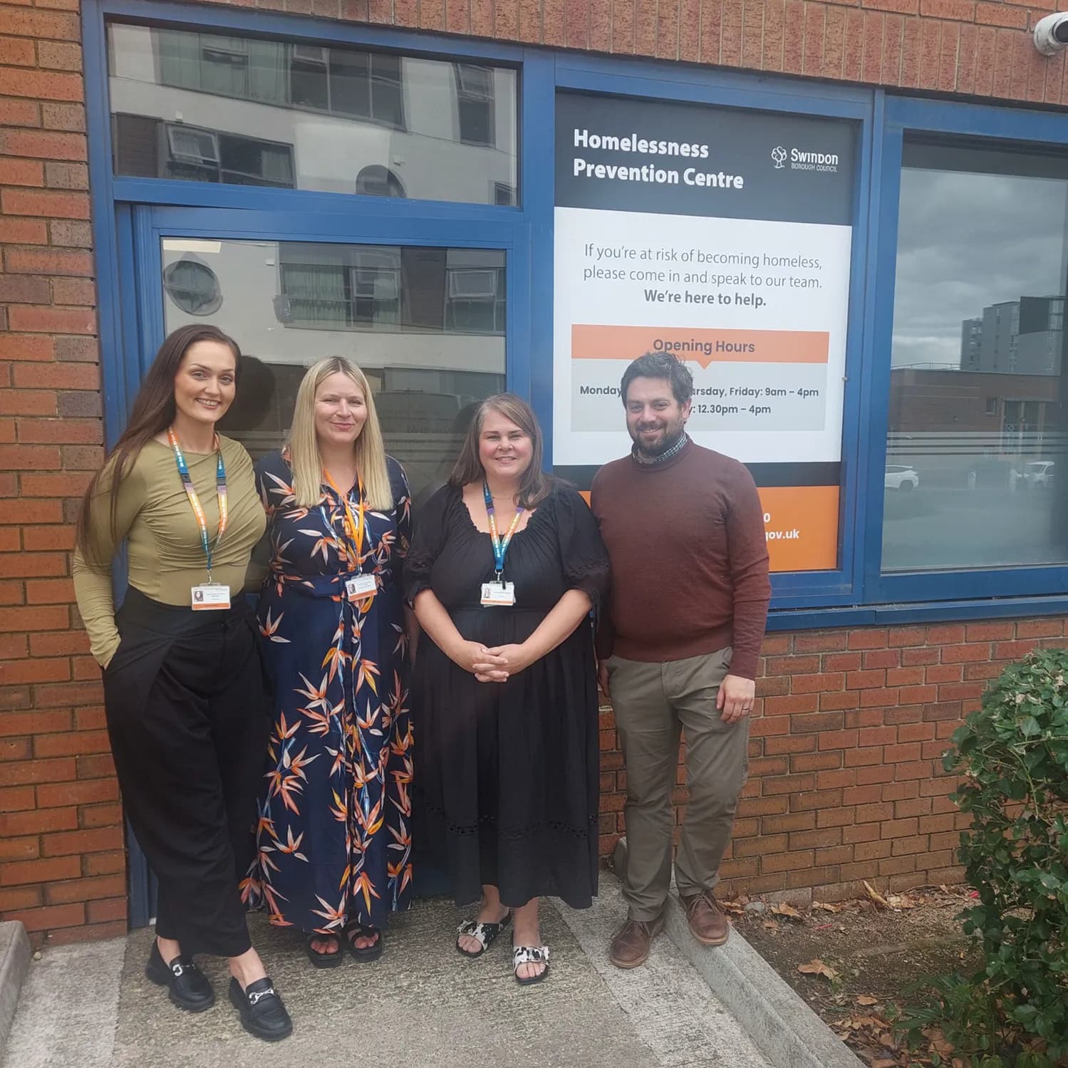 Four adults, three women and one man, standing in front of the Homelessness Prevention Centre with a sign visible in the window.